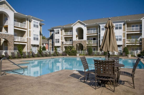 Apartment complex swimming pool with patio seating and umbrella