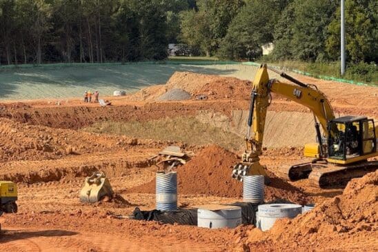Excavator digging trench with concrete pipes at construction site
